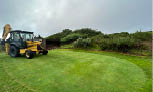 A yellow tractor is on a green field, digging up the grass. AI generated content